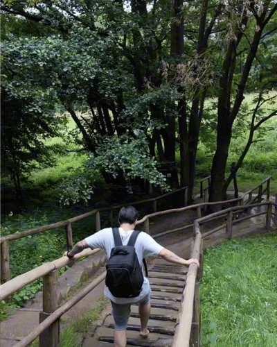 Besucher läuft barfuß über eine Holztreppe, die mit Schlamm gefüllt ist. Sie befindet sich auf dem Barfußpfad am Hohen Meißner. Die Treppe ist von grüner Natur und Bäumen umgeben.