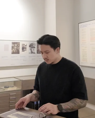 Besucher betrachtet historische Dokumente in der Dauerausstellung der Gedenkstätte Trutzhain. Im Hintergrund sind Ausstellungstafeln mit Fotografien aus der NS-Zeit zu sehen.