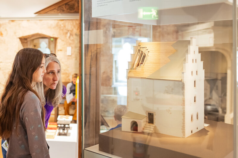 Eine Familie mit zwei Erwachsenen und zwei Kindern betrachtet interessiert ein Architekturmodell in einer Glasvitrine im Museum.